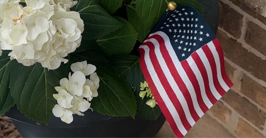 Small American flag placed in a planter with white hydrangea flowers.