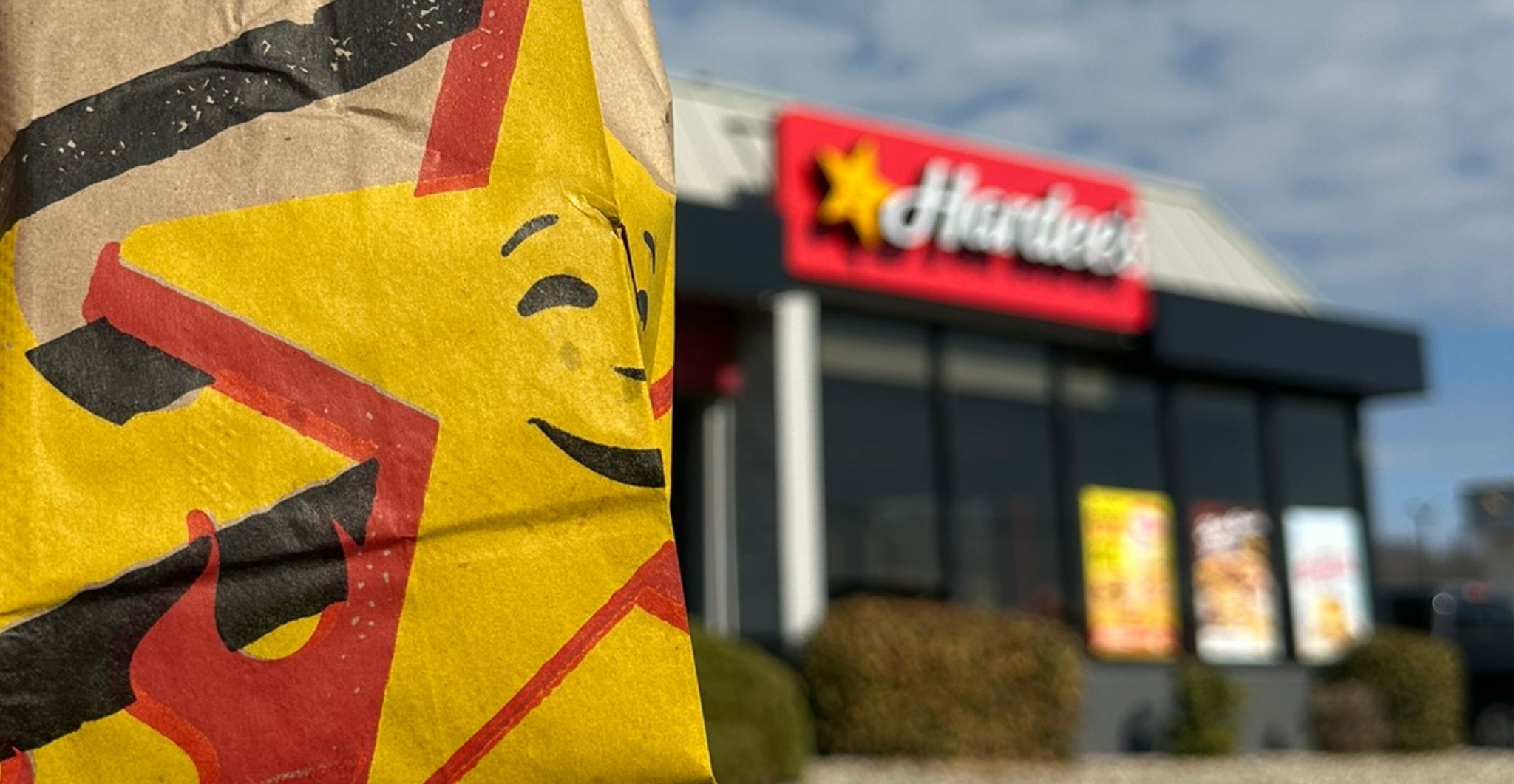 Close-up of a Hardee’s Stars for Heroes bag with a Hardee’s restaurant in the background.