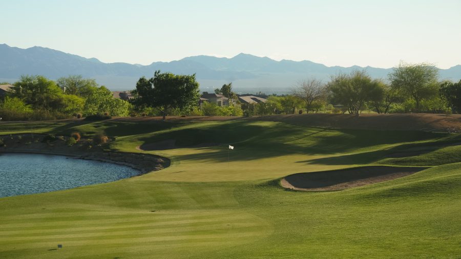 TPC Las Vegas golf course featuring a green beside a water hazard with desert landscaping and mountain views in the background