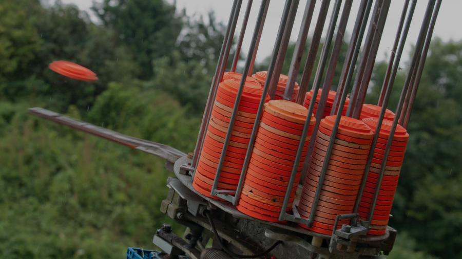 Skeet shooting clay targets stacked on a launcher with an orange clay disc flying through the air at an outdoor shooting range